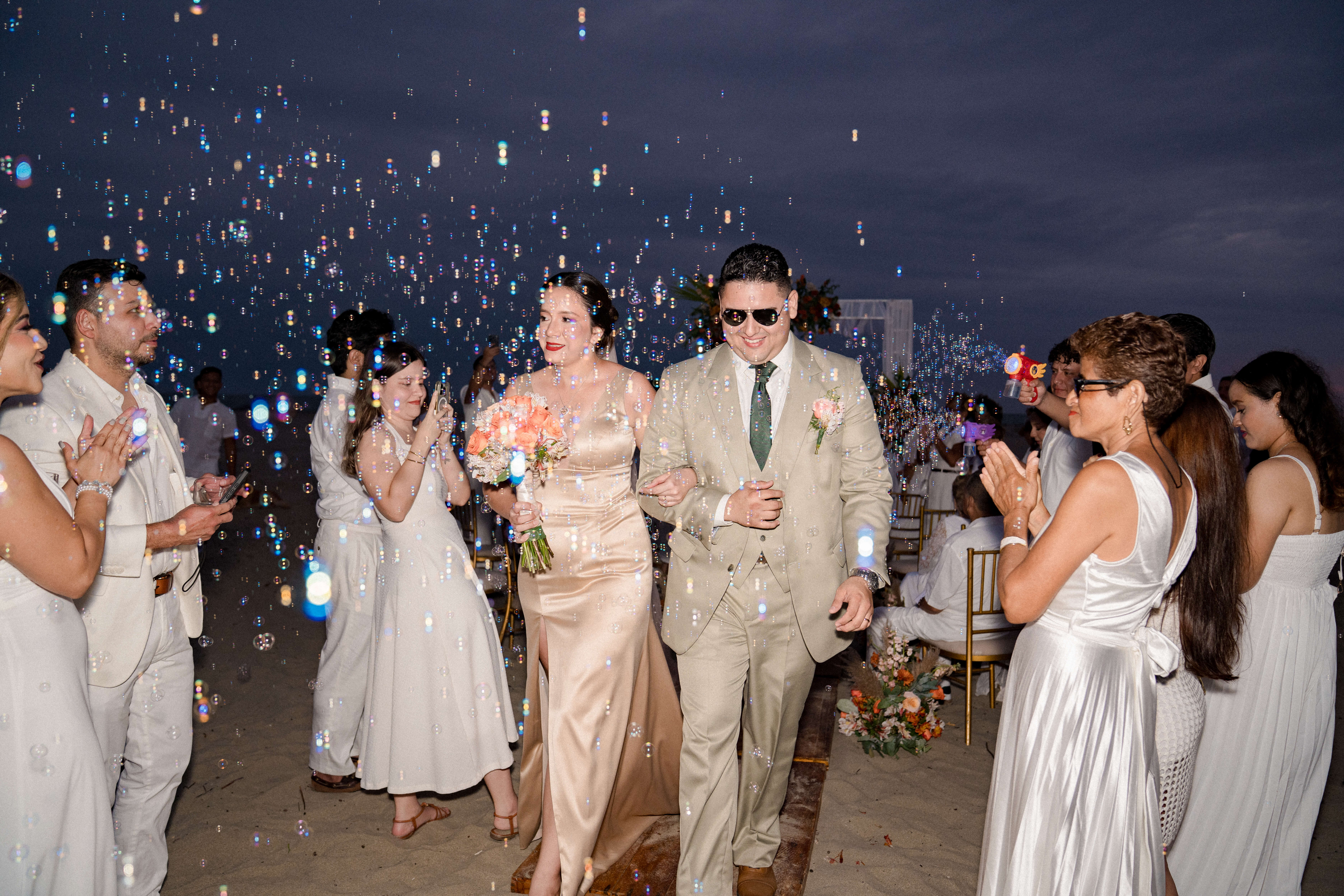 Novios Mark y Allison caminando tomados de la mano en la playa de Playas Ecuador, velo al viento y ramo de rosas, boda en Chalet Suizo